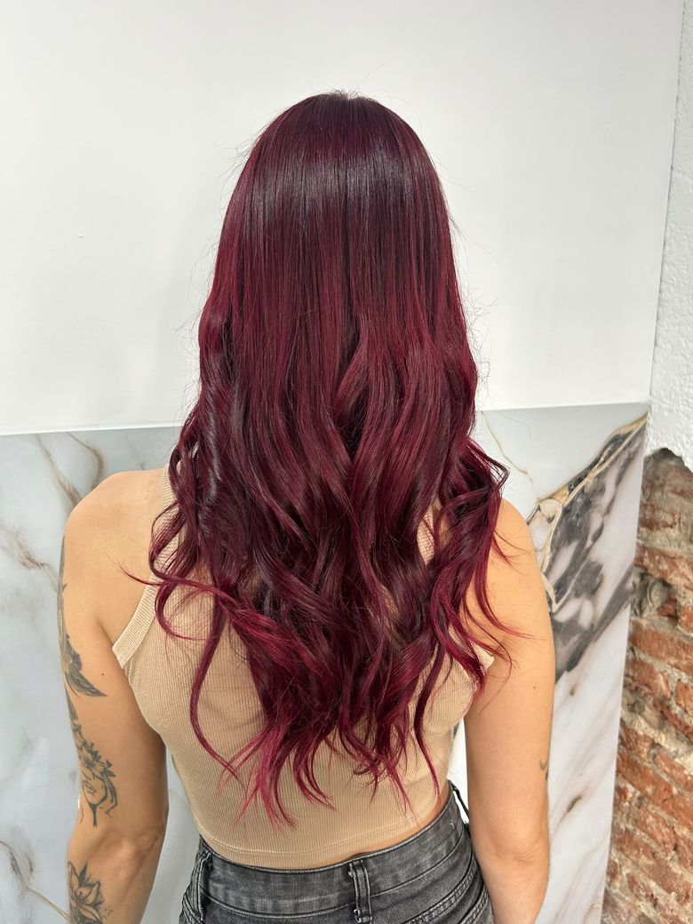 Color bordó en pelo largo con ondas, de espaldas contra la pared de mármol
