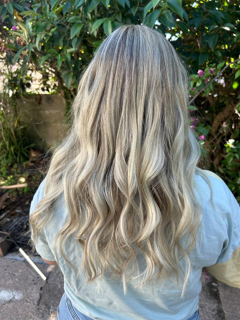 Mechas rubio ceniza en pelo largo con ondas, de espaldas al aire libre
