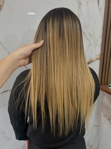 Progresivo en pelo largo con mechas rubias miel, lacio y brillante, de espaldas contra la pared de mármol